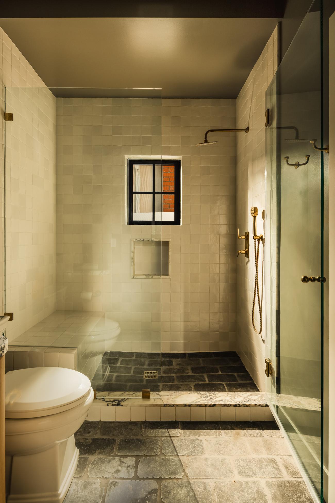 Moody guest bath shower in dark charcoal tile with brass fixtures
