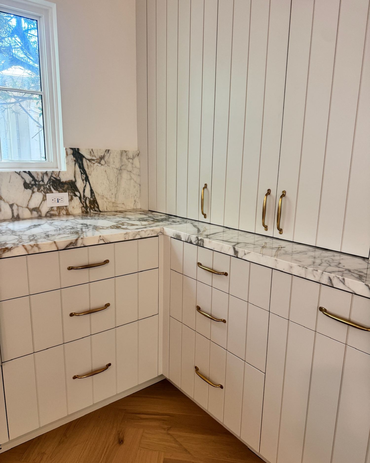 Butler's pantry with white paneled cabinetry, brass hardware, and marble countertop and backsplash