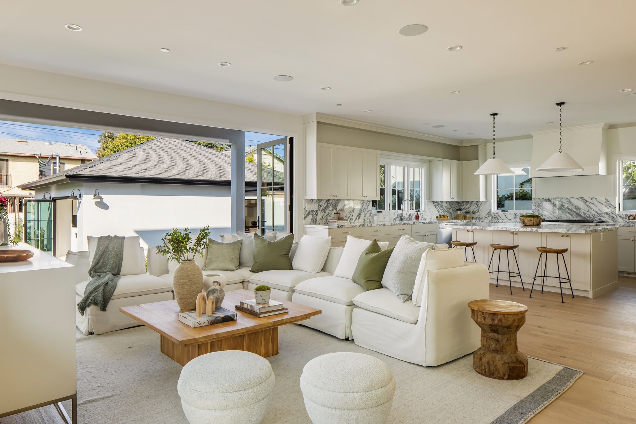 Open living room and kitchen at Greenfield, white cabinetry and marble backsplash with the wall opened to the yard