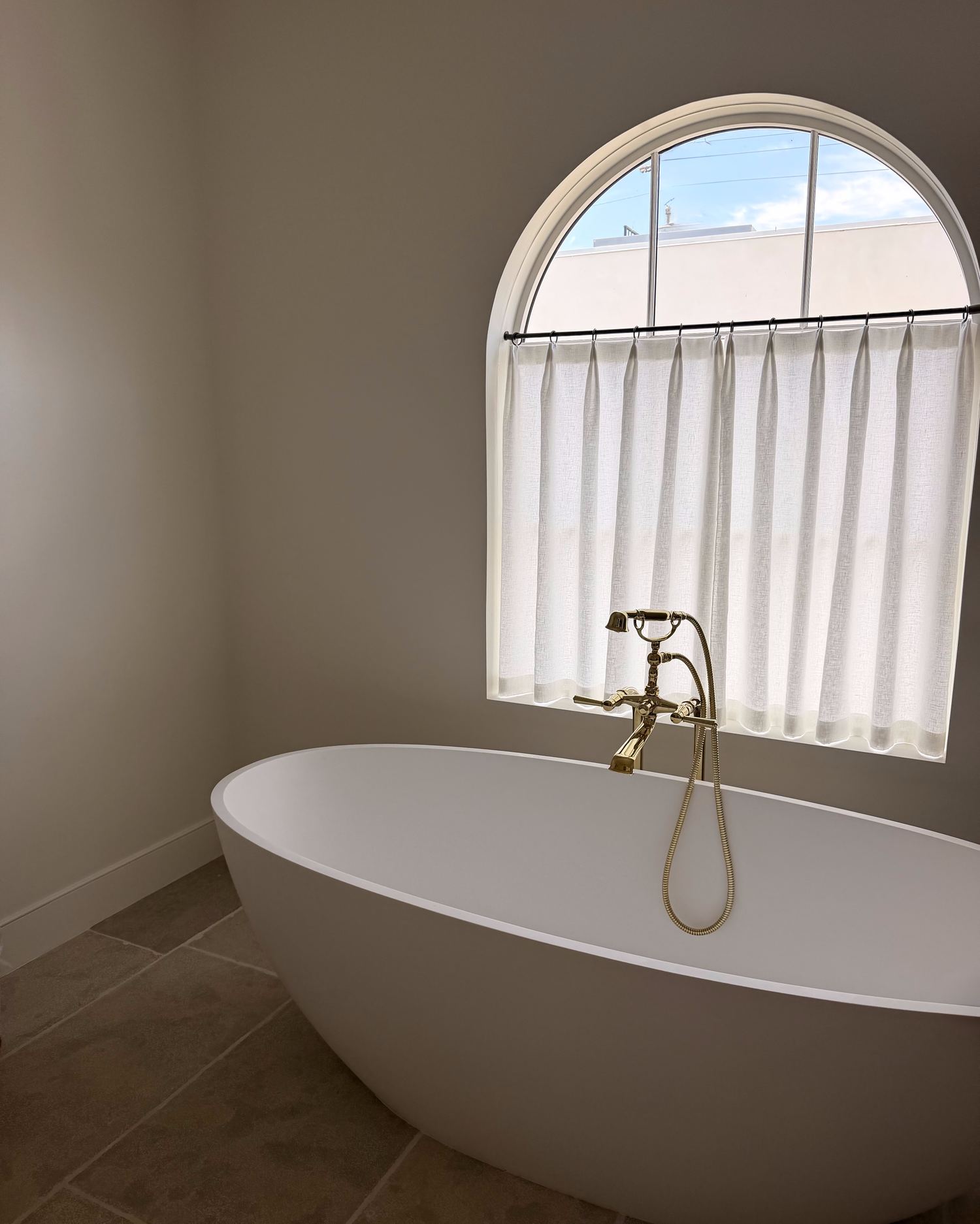Primary bath with freestanding tub beneath an arched window and brass fixtures